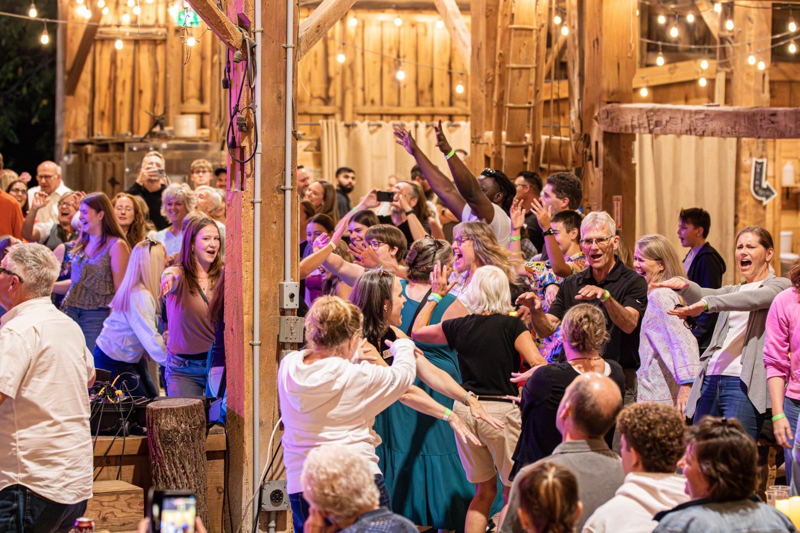 A crowd dancing and raising their hands beneath warm string lights.